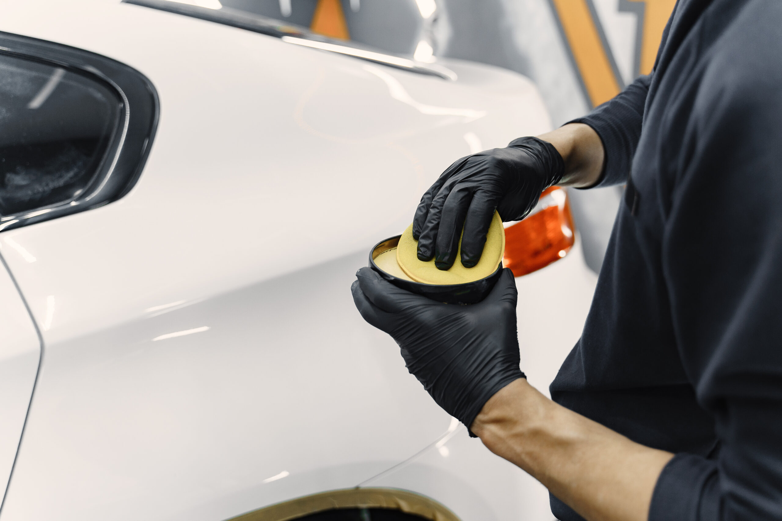 Man polish a car in a garage Man in a garage. Worker polish a car. Man in a black uniform.